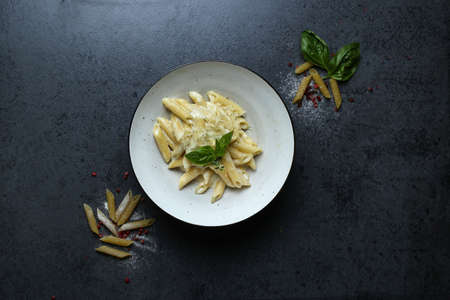 The top view of a plate of pasta with cheese sauce and basil on the black tableの写真素材