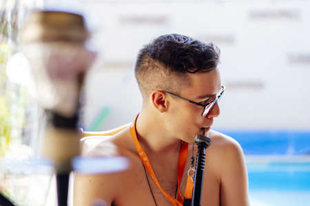 A young male smoking a hookah next to the pool in summerの写真素材