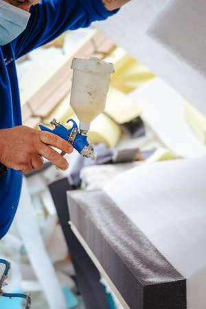 A vertical shot of a furniture maker spraying upholstery adhesive over a prepared foam