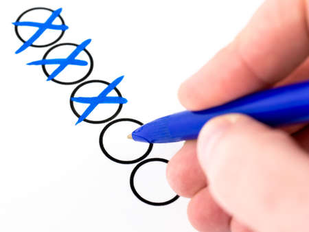 A closeup shot of hand with blue ballpoint pen marking check boxes
