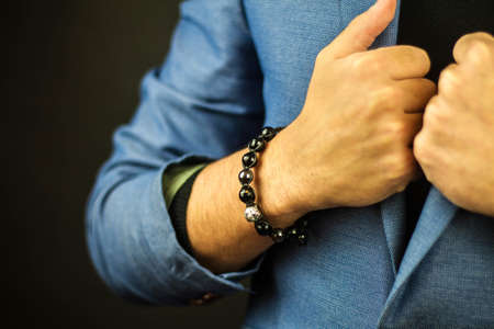 A closeup shot of a man in a suit wearing a beautiful bracelet made of stones