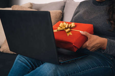 A closeup of a woman talking to her friends on a laptop and showing them a red gift box