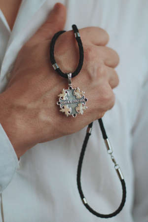 A closeup shot of a male holding a charm necklace with a silver pendant and a black cord