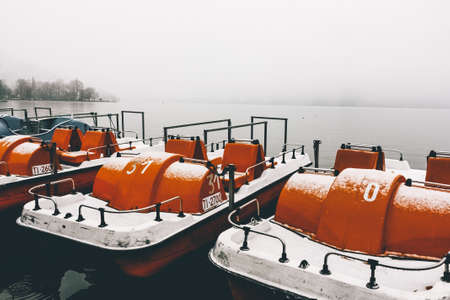The orange paddleboats by the pier on a calm lake captured on a foggy winter dayの写真素材