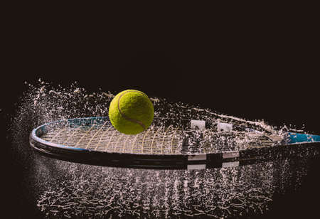 A closeup shot of a tennis ball and racket with a splash of water isolated on a dark backgroundの写真素材