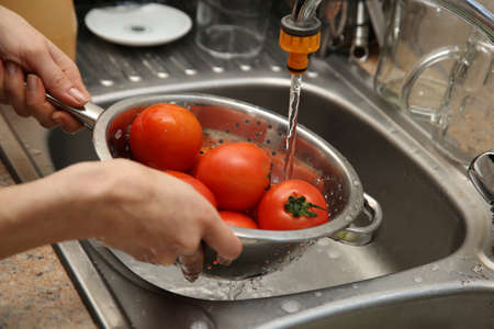 A women using a colander and a kitchen sink to wash tomatoes. Food hygiene and safety concept image.の写真素材