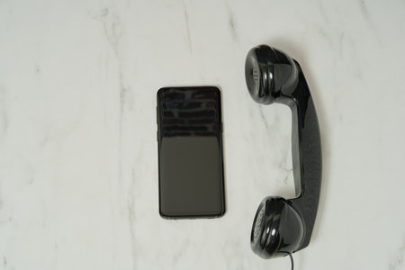 A closeup shot of a black phone handset and a black smartphone on a white table background
