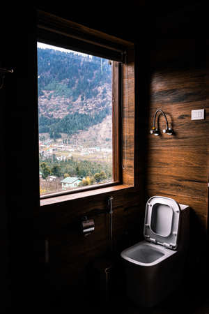 A vertical shot of a toilet seat by the window with the beautiful view of a landscape in the backgroundの写真素材