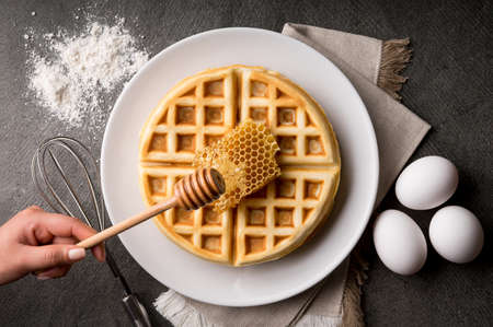 A high angle shot of a person making waffles with honey in a kitchen