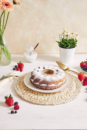 A vertical shot of a ring cake with fruits and powder on a white table with white background