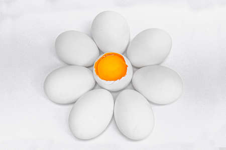 A top view shot of eggs placed around one cracked egg showing the yellow yolk inside to mimic a blossoming flowerの写真素材