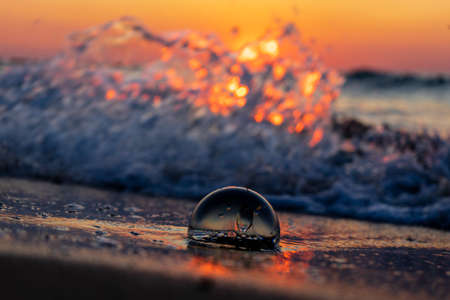 A selective focus shot of a glass ball on the beach at sunsetの写真素材