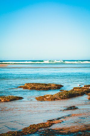 A beautiful vertical shot of vibrant blue ocean waves around the rocky beach