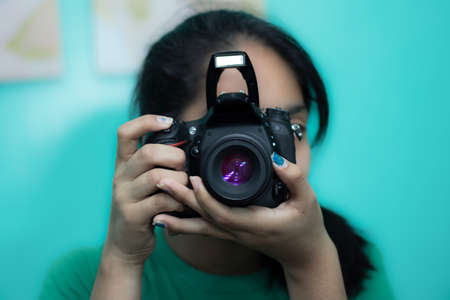 A young female photographer taking a picture with a DSLR camera against a blue backgroundの写真素材