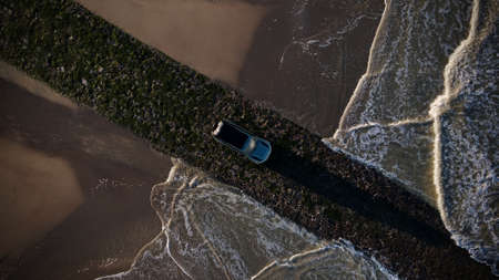 An aerial view of a car driving through a paved road extending over the seaの写真素材