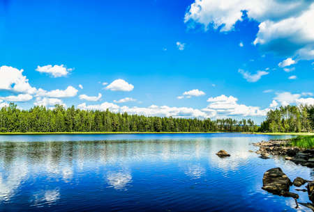 The reflection of the clouds and the blue sky in a calm lake surrounded by trees in Swedenの写真素材