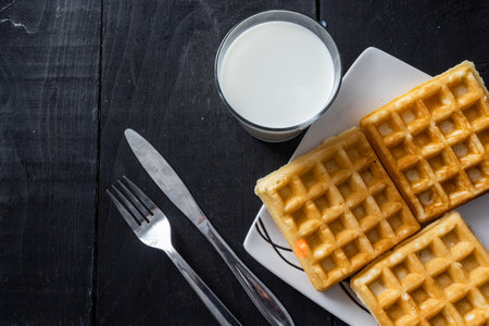 A closeup shot of square waffles and milk glass on a wooden table backgroundの写真素材