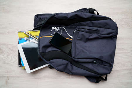 A top view of a backpack with a tablet, phone, headphones, notebooks, and pens