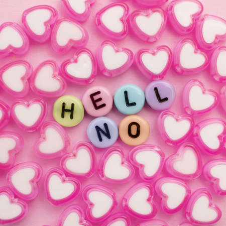 Some plastic beads with letters form the words "HELL NO" and there are some pink heart beads around it. Background is pink.の写真素材