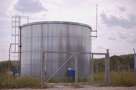 A closeup of a large water tank on a grassy landscape against a cloudy skyの写真素材