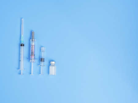 A top view closeup of a group of syringes and vaccine bottles isolated on blue background