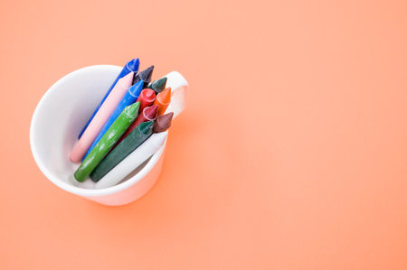 A top view of the colorful crayons in the cup on the orange surface - space for textの写真素材