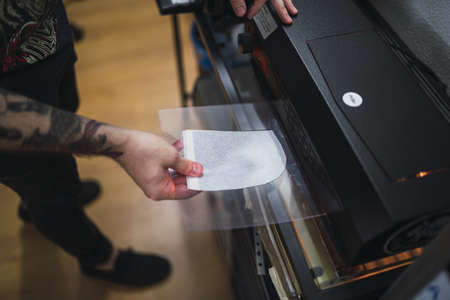 A high angle shot of a tattoo artist working with a lamination machine