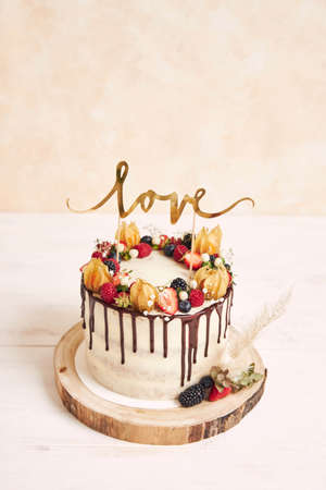 A vertical shot of a beautiful wedding cake with fruits chocolate drip and with Love topperの写真素材