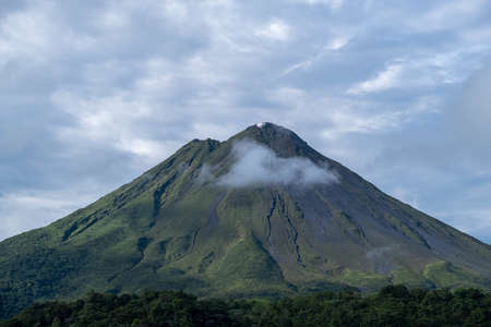 A shot of a breathtaking giant mountain covered in forests, gleaming under the cloudy skyの写真素材