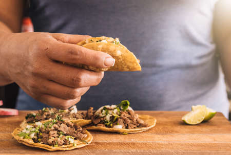 Hispanic woman holding taco with yellow corn tortilla, pork, onion and salsa at Mexico. Mexican street tacos.の写真素材