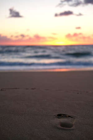 The human footprint on the sandy beach gleaming under the sunsetの写真素材
