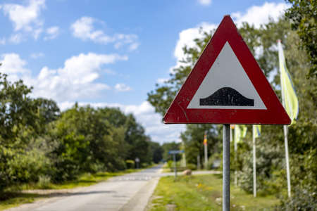 Triangle traffic sign on the side of a country road warning there is a threshold coming up in the road. Symbol against a blue sky with clouds and treeの写真素材