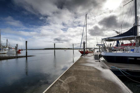 An eye-level shot of sailboats in a port under the blue cloudy sky in Tin Can Bay, Queensland, Australiaのeditorial素材