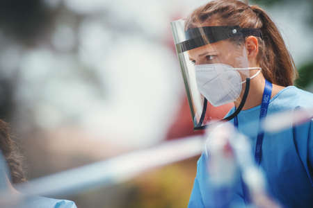 BRNO, CZECH REPUBLIC - Apr 24, 2020: Female health care worker with a respirator and a plastic face shield standing on the street.のeditorial素材