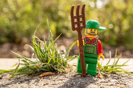 POZNAN, POLAND - May 03, 2020: Lego farmer figurine holding a pitchfork while standing next to green...