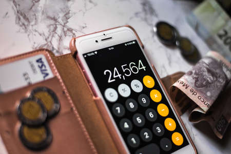MEXICO CITY, MEXICO - Mar 31, 2020: A closeup of a phone with the calculator app on it with mexican pesos and visa credit card under the lights.のeditorial素材