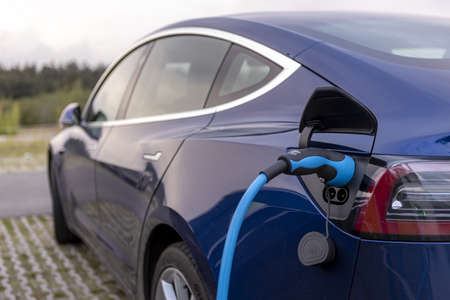 HOGE HEXEL, NETHERLANDS - Aug 30, 2020: Closeup of blue modern design electric Tesla car charging in parking lot with electric charge cable sticking outのeditorial素材