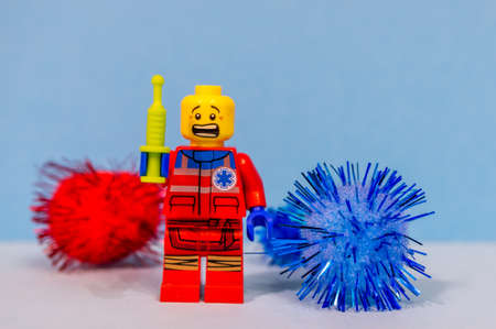 POZNAN, POLAND - Nov 28, 2020: Scared Lego doctor figurine holding a vaccine next to corona virus