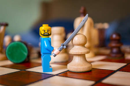 POZNAN, POLAND - Feb 15, 2021: Lego man toy figurine holding up a sword in front of a chess piece on a board.のeditorial素材