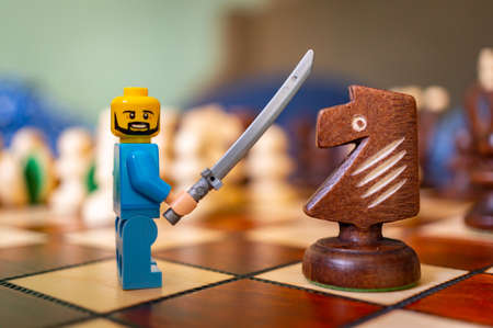 POZN, POLAND - Feb 15, 2021: Lego man toy figurine holding up a sword in front of a knight chess piece on a board.のeditorial素材