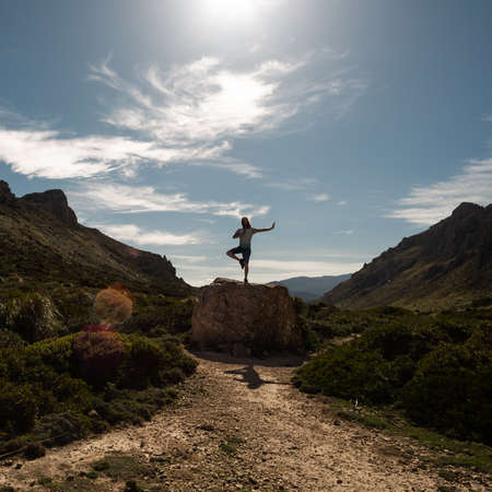 PORT DE POLLENCA, PORTUGAL - Mar 06, 2020: Man doing yoga on top of a rock in a valley with te sun on top of himのeditorial素材