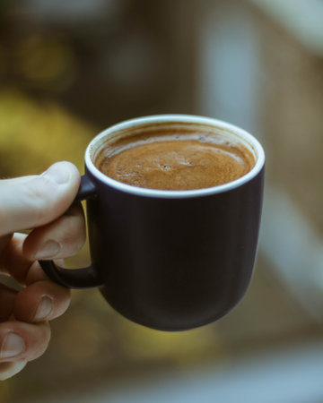 A closeup shot of a person holding a black cup of coffee with a blurry background