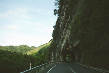 The mesmerizing view of the road through the rock cliff arch surrounded by trees and mountains