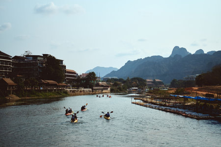 The Nam Xong River surrounded by buildings and rocks under the sunlight in Vang Vieng in Laosの写真素材