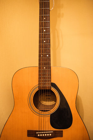 A vertical closeup of an acoustic guitar against a wall under the lights
