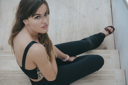 A high-angle shot of an attractive brunette girl staring up while sitting on the stairs
