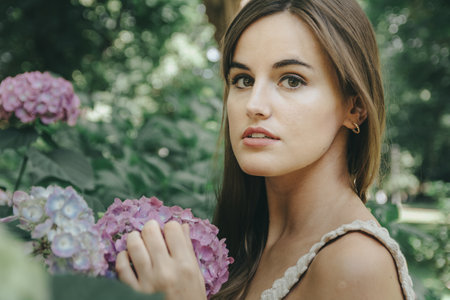 An attractive girl with brown long hair posing near the purple flowers in the garden
