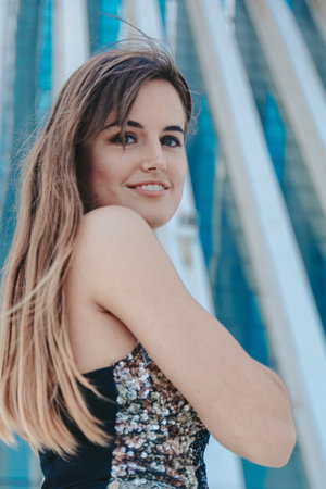 An attractive girl with brown long hair posing in front of the modern building