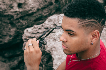 A beautiful shot of a young man taking his sunglasses off  while sitting on the rocks near the lake