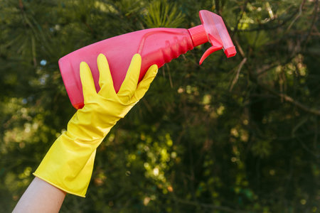 A female with yellow gloves holding a plastic cleaning spray bottle - plastic pollution concept